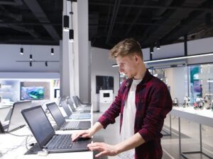 A young man chooses a laptop in an electronics store. A man looks at laptops in the computer department at the technology store. Buy a laptop A young man chooses a laptop in an electronics store. A man looks at laptops in the computer department at the technology store. Buy a laptop