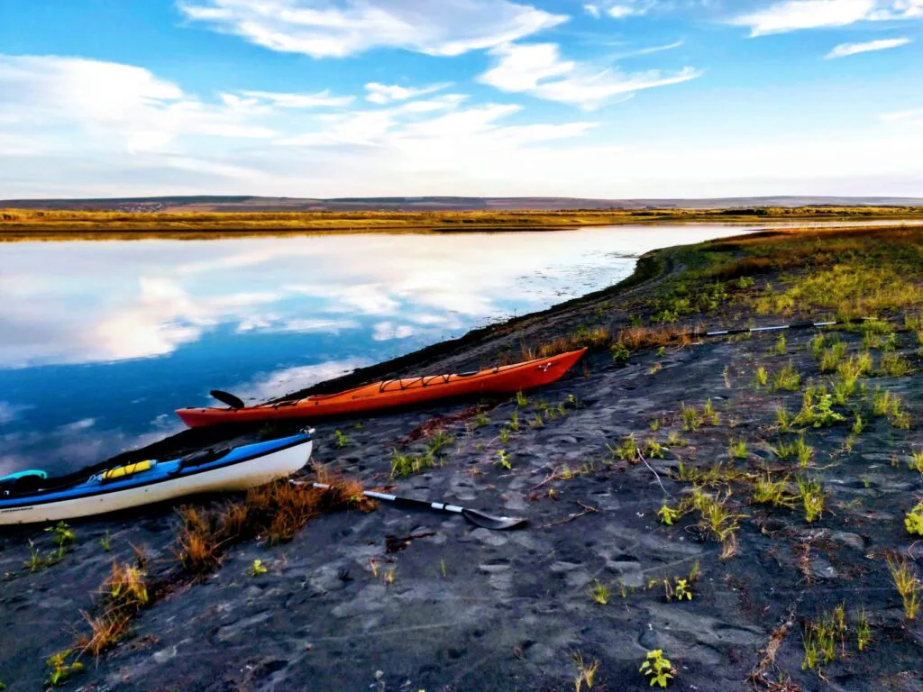 Sunny blue sky reflecting off surface of Potholes Reservoir in eastern Washington, with two kayaks resting on the lake shoreline.