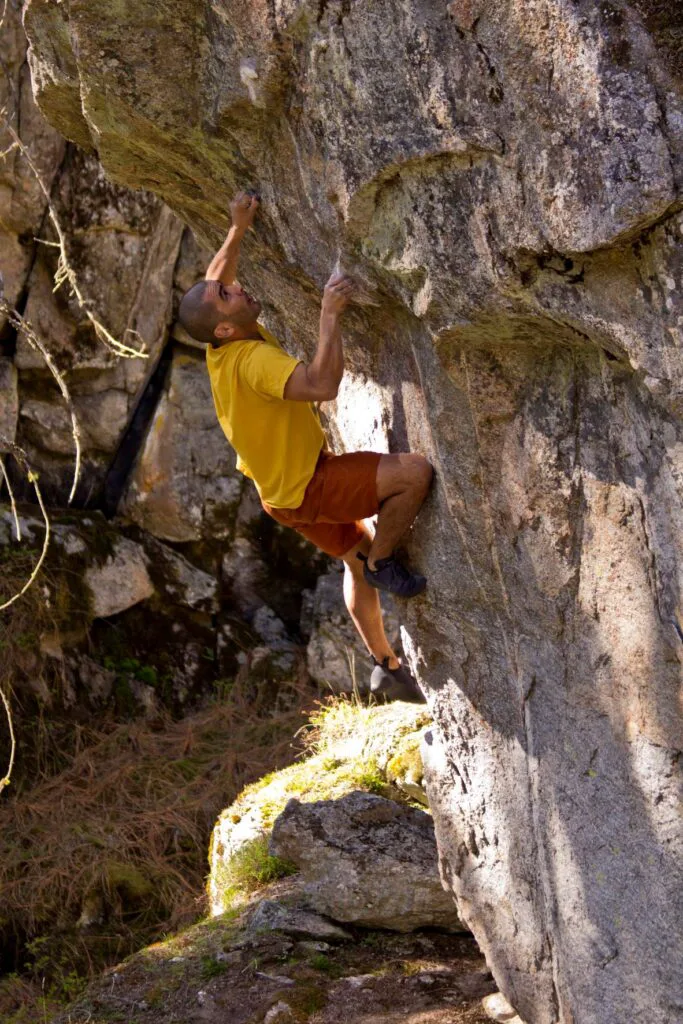 Man named Arden Pete, wearing yellow shirt and red pants and climbing shoes, rock climbing the Middle Finger of Fury at McClellan in Spokane.