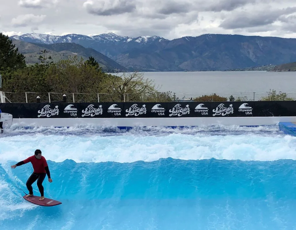 Man shredding a wave at Lakeside Surf in Lake Chelan, WA -- man on surfboard crossing a wave, with view of Lake Chelan in the far background.
