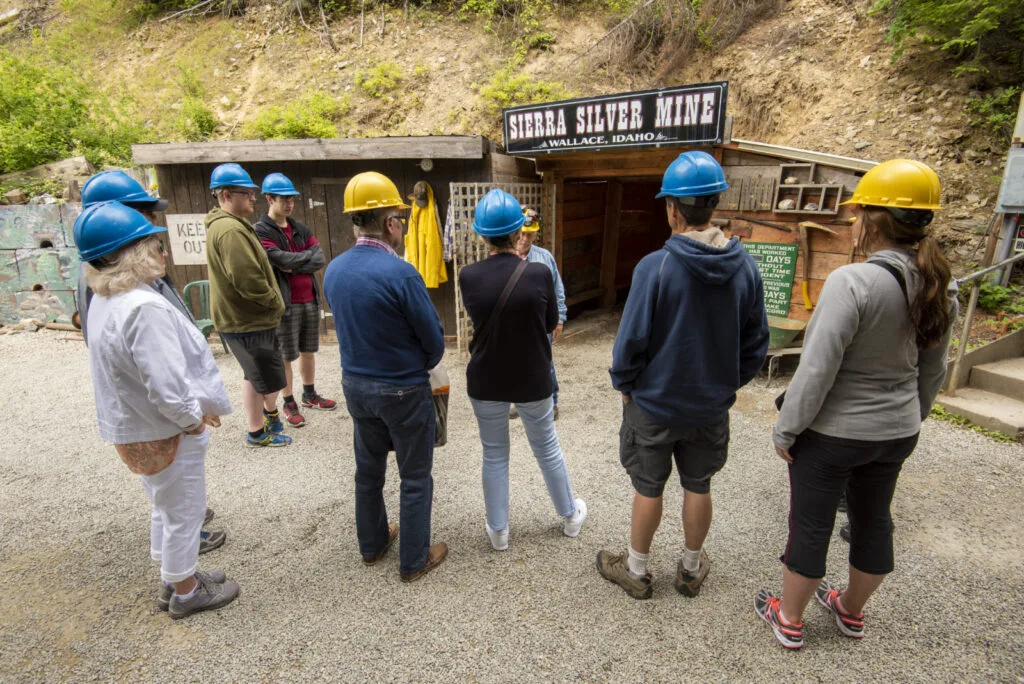 Group of tourists wearing blue and yellow hardhats stand at the entrance to the Sierra Silver Mine ready to begin their tour.