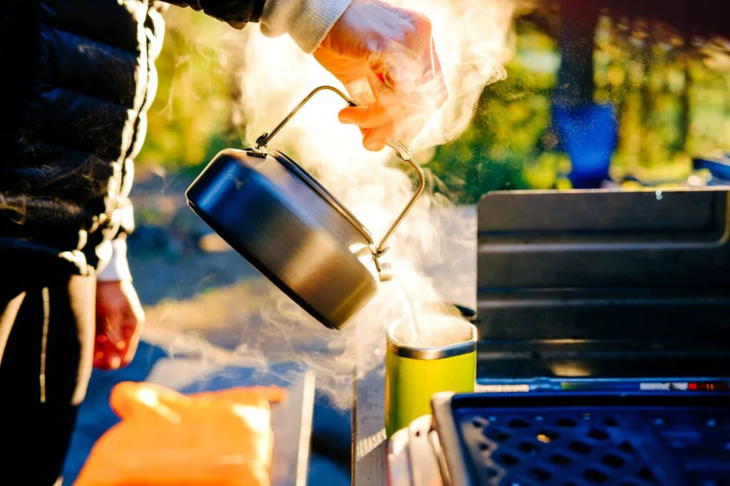 Campsite kitchen with a person pouring a kettle of hot, steamy .water into a mug