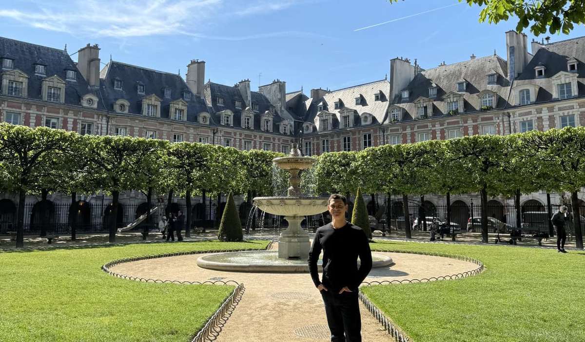 Nomadic Matt standing in the Place de Vosages, a large enclosed square surrounded by buildings, with a fountain in the middle, in Paris, France