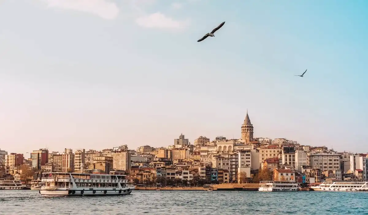 A view of ferries on the Bosphorus River at sunset, with Galata Tower rising above the Istanbul skyline