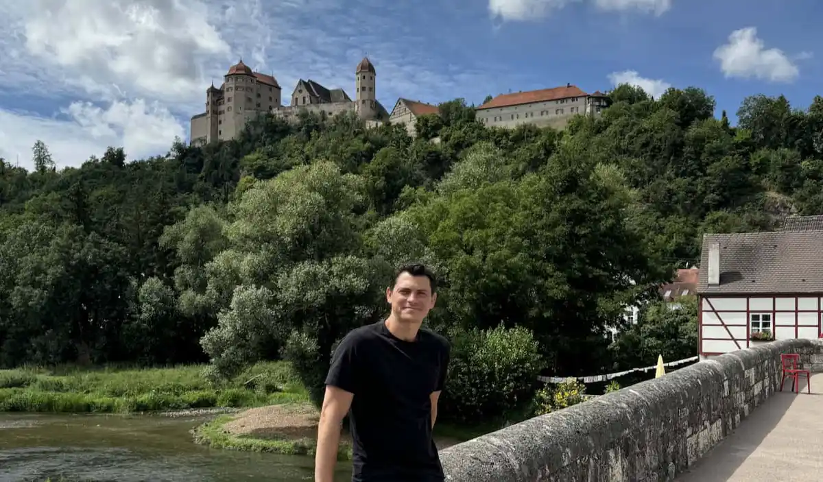 Nomadic Matt posing on a bridge in Europe with a towering castle in the background