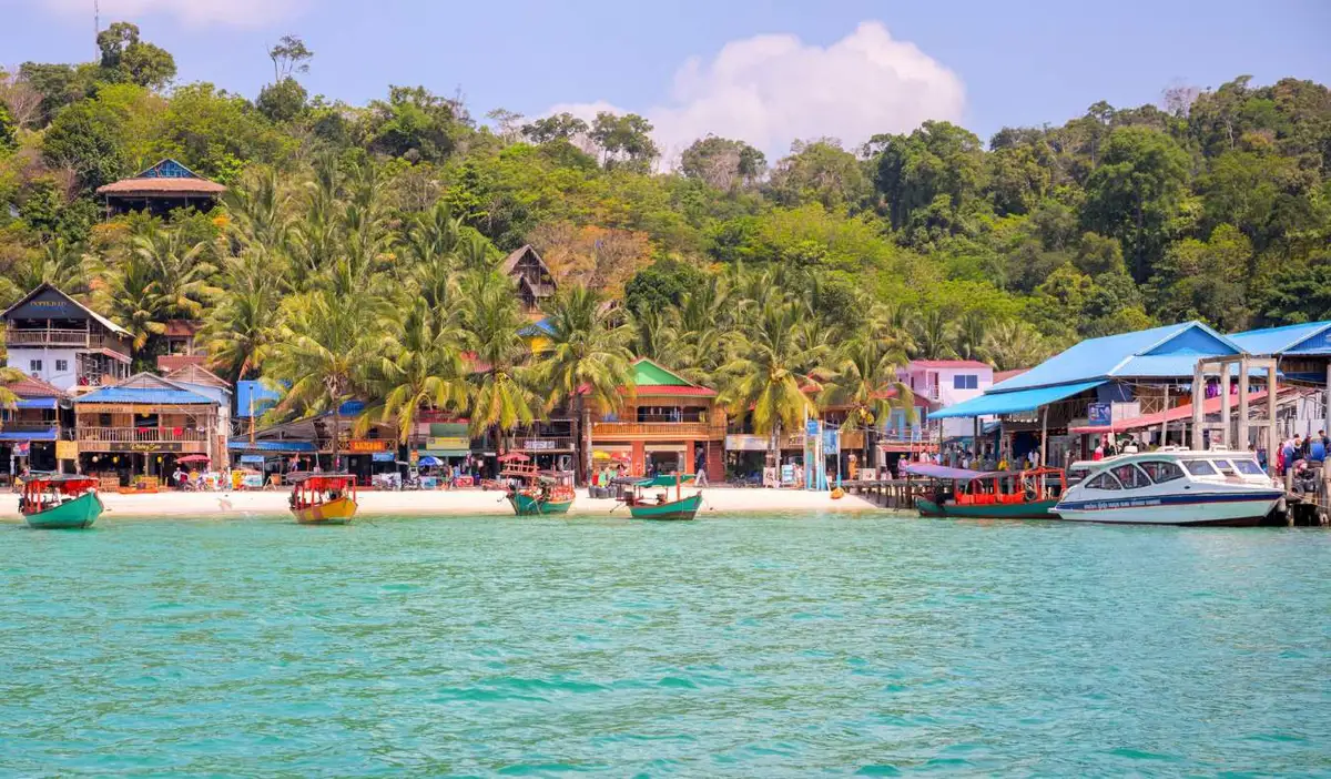 A beach with wooden huts and buildings with boats docked off the shore in Koh Rong, Cambodia