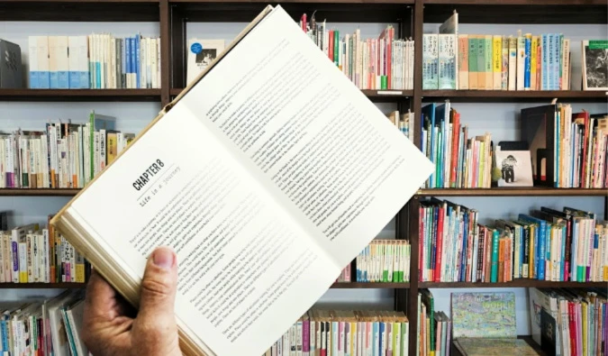 A man holding an open book in front of a large bookshelf