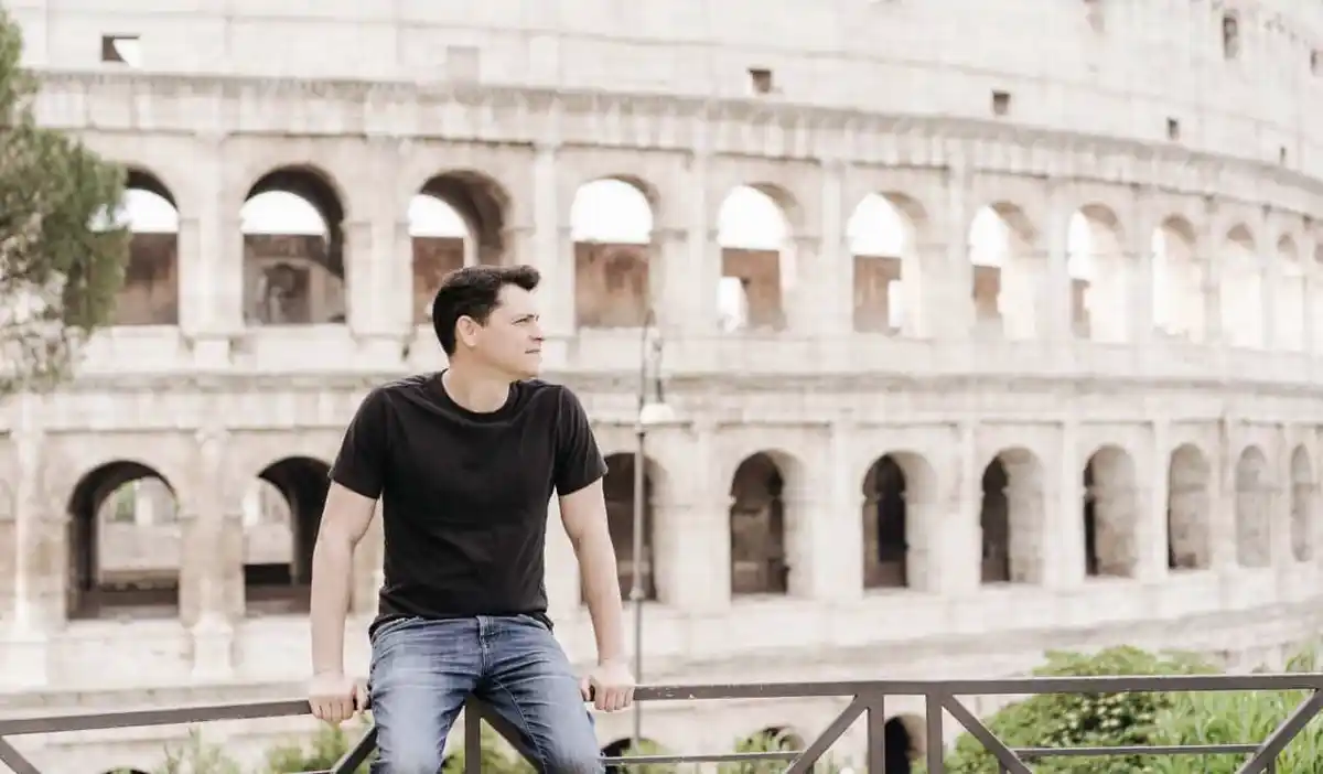 Nomadic Matt posing for a photo near the massive and ancient Roman Colosseum in Rome, Italy