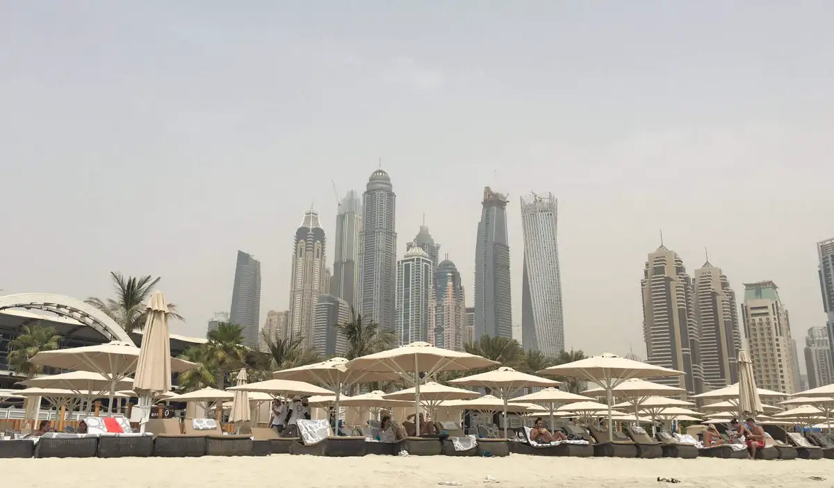 A row of lounge chairs and umbrellas on a beach with the tall skyscrapers of Dubai in the background
